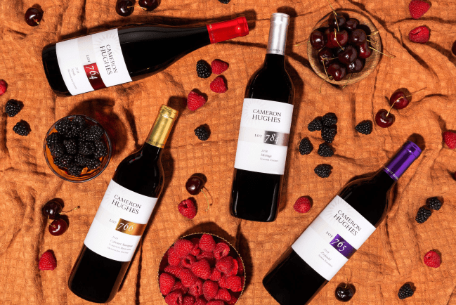 Four Cameron Hughes Wine bottles on an orange banket with berries and cherries scattered around them.