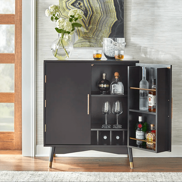 A half-open black bar cabinet filled with barware and topped with glassware