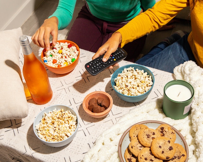 Someone holding a remote near a table covered with snacks