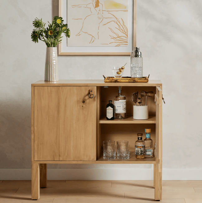 A half-open bar cabinet made of wood and stocked with barware