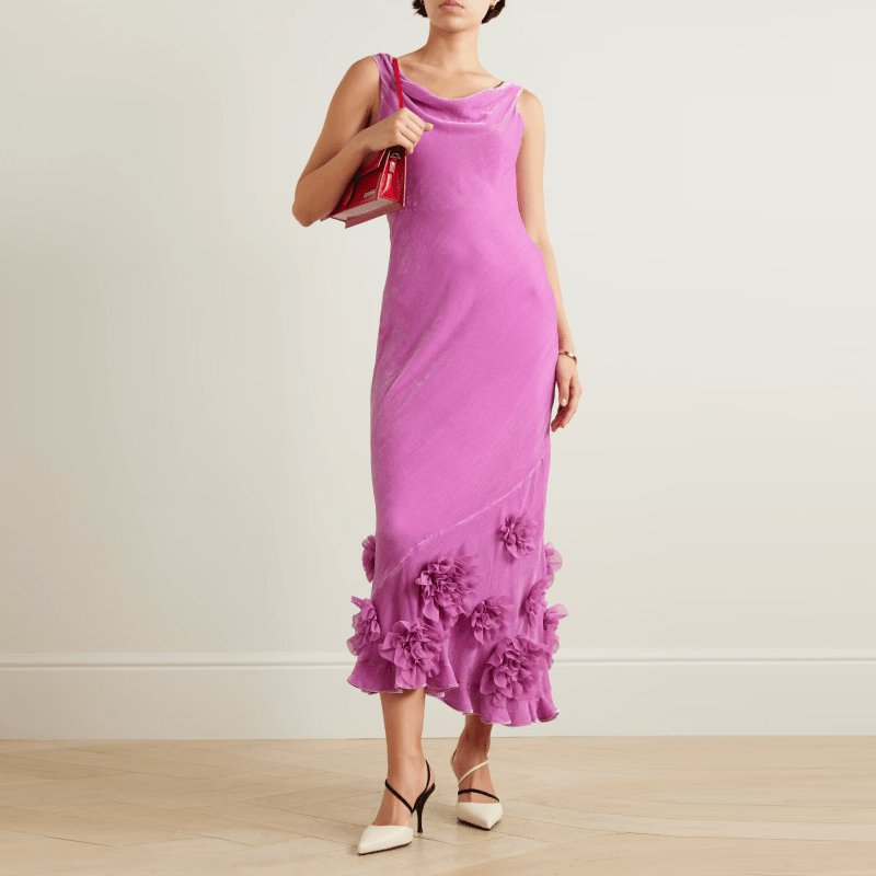 A model wearing a fuschia velvet cowl-neck slip dress with floral appliques on the skirt