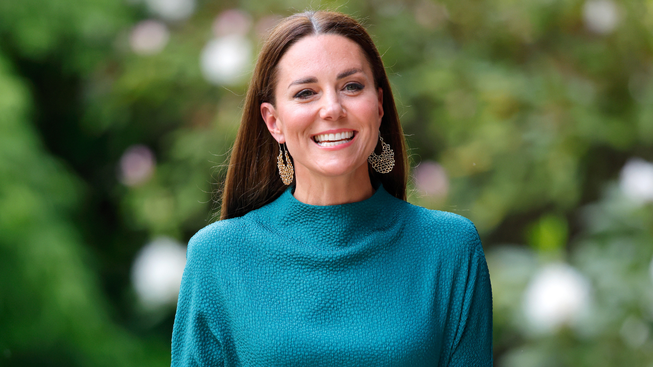 Kate Middleton, a white woman in a blue dress smiles for the camera.