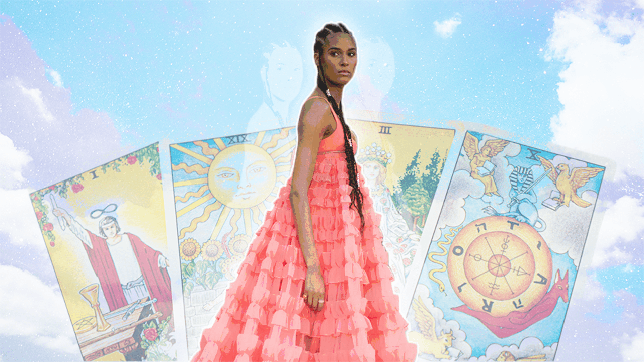 A woman in a pink dress standing in front of a deck of Tarot cards laid out for her reading & horoscope this week