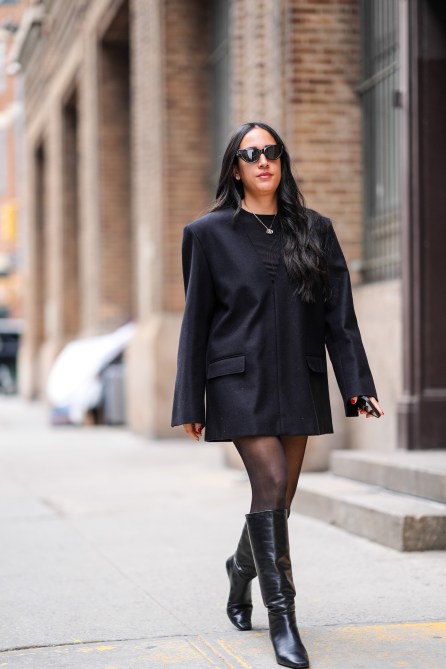 A guest wears a black oversized blazer dress, tights, and black leather boots, during NYFW, on February 10, 2024 in New York City.