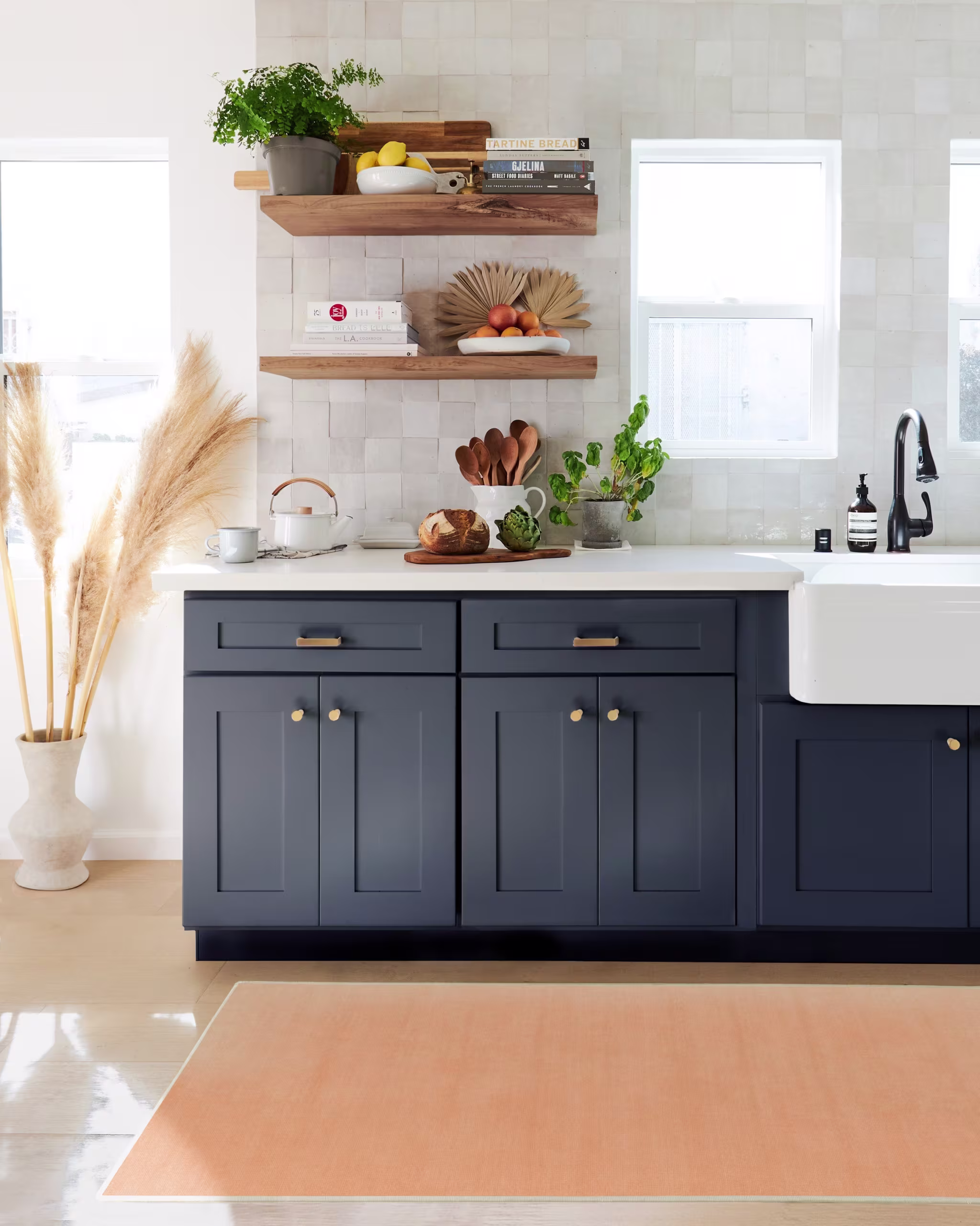 A peach-colored rug in a kitchen with navy blue cabinets, white countertops, and gray tiled walls.