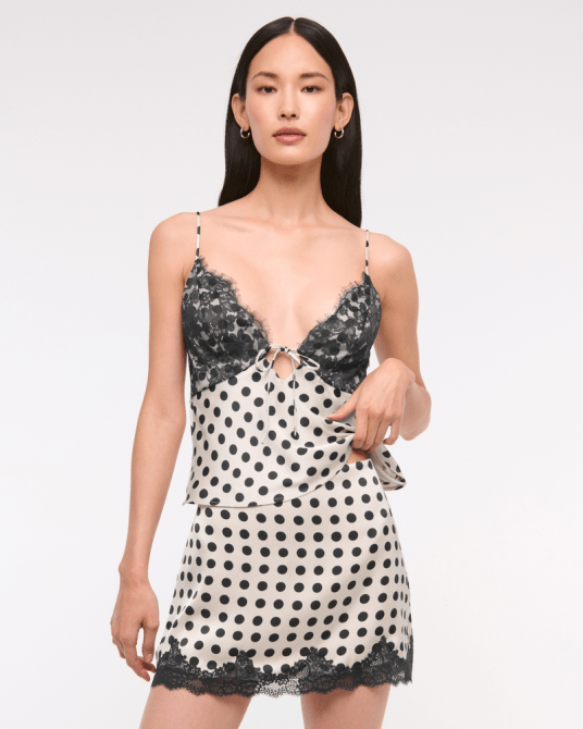 A model wearing the Abercrombie & Fitch High Rise Satin Lace-Hem Mini Skirt in a cream polka dot pattern