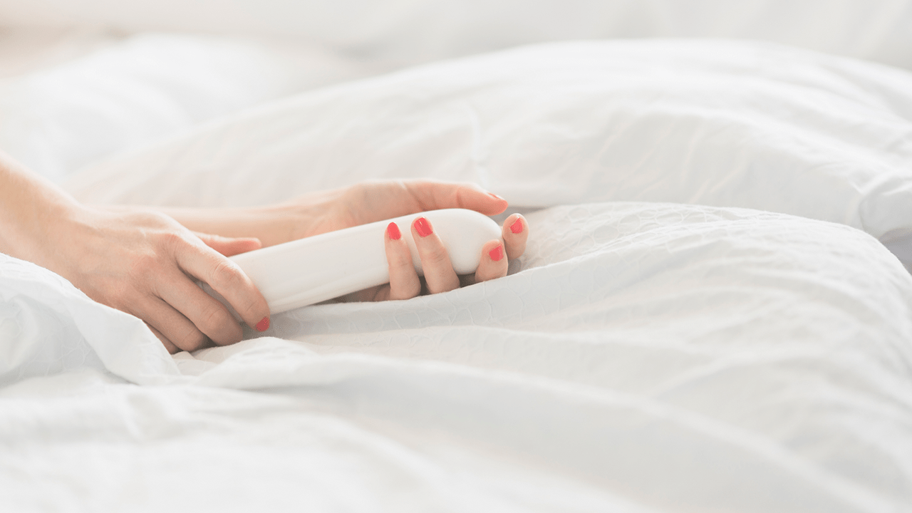 A woman's hand holding a sex toy in bed.